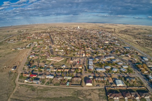 Aerial view of a small town with houses, roads, and open fields under a partly cloudy sky.