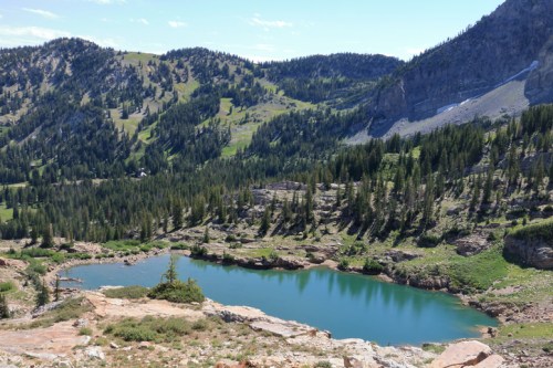 A serene mountain landscape featuring a clear blue lake surrounded by lush greenery and rugged hills.