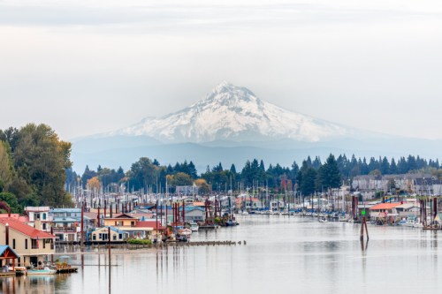 A scenic view of a harbor with boats, colorful buildings, and a snow-capped mountain in the background.
