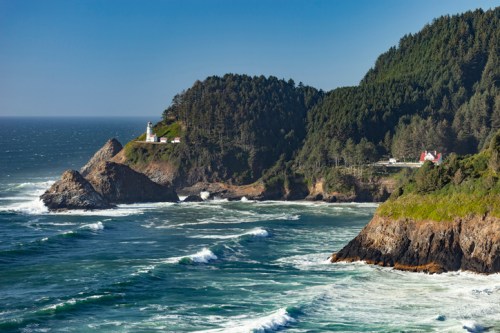 A scenic coastal view featuring a lighthouse on a cliff, surrounded by lush greenery and crashing ocean waves.
