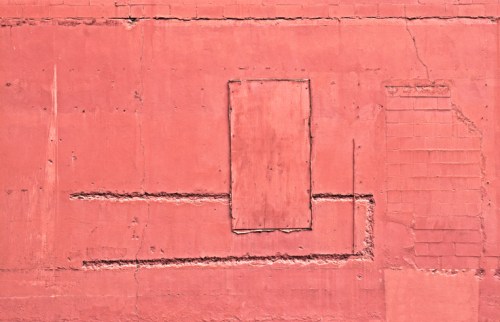 A textured pink wall with a boarded-up window and uneven patches, showcasing wear and age.