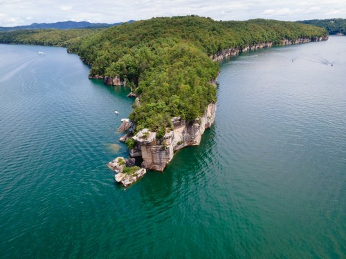 Aerial view of a lush green island with rocky cliffs surrounded by calm blue water.