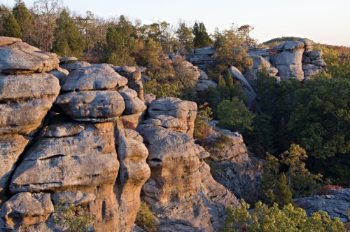 Rocky cliffs surrounded by trees at sunset, showcasing natural formations and a serene landscape.