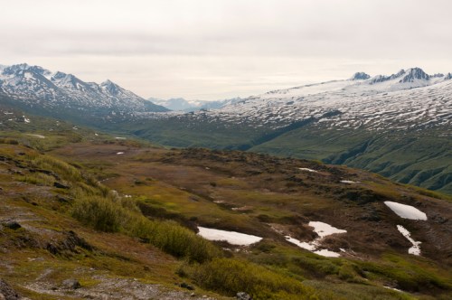 A scenic view of mountains with snow-capped peaks and a lush green valley under a cloudy sky.