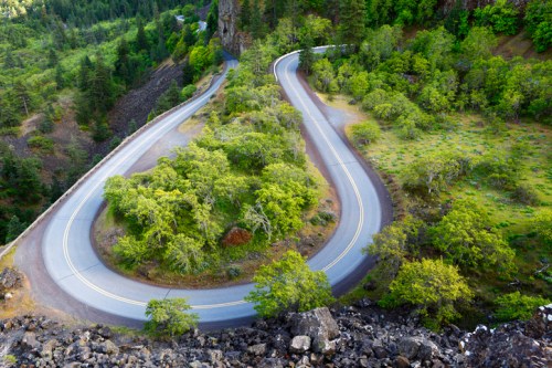 Winding road through lush greenery, surrounded by trees and rocky terrain, viewed from above.