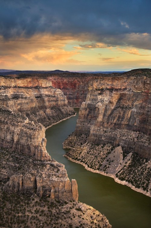 A winding river flows through a dramatic canyon under a colorful sky at sunset.