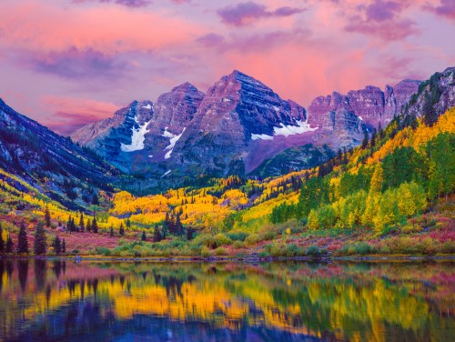 A vibrant landscape featuring mountains, colorful autumn trees, and a serene lake reflecting a pink and purple sky.