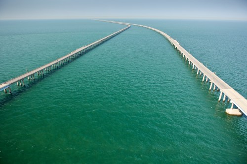 Aerial view of two long piers extending into calm blue waters, creating a striking geometric pattern.