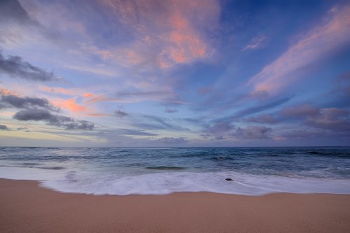 A serene beach scene at sunset, with soft waves lapping at the shore and colorful clouds in the sky.