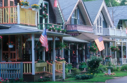 Colorful Victorian-style houses with porches, flower boxes, and American flags, lined along a charming street.