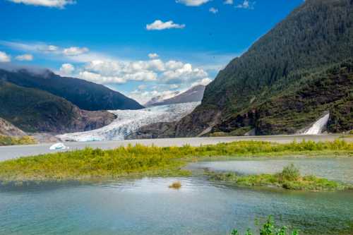 A stunning landscape featuring a glacier, mountains, and a serene lake with lush greenery in the foreground.