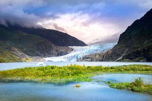 A stunning glacier flows down from mountains into a serene lake, surrounded by lush greenery and dramatic clouds.