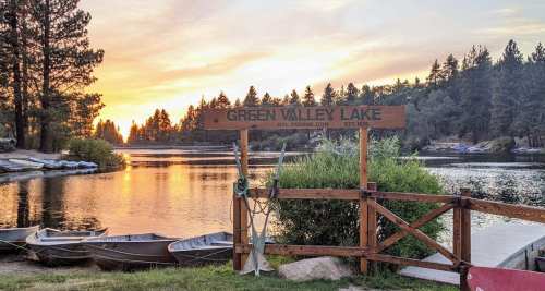 Sunset over Green Valley Lake, with a wooden sign and rowboats by the shore, surrounded by trees.