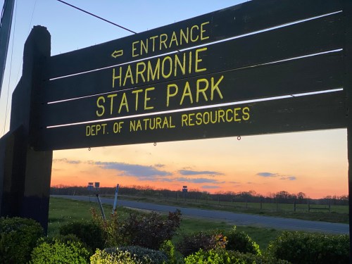 Sign for Harmonie State Park at sunset, with directional arrow and "Dept. of Natural Resources" below the park name.