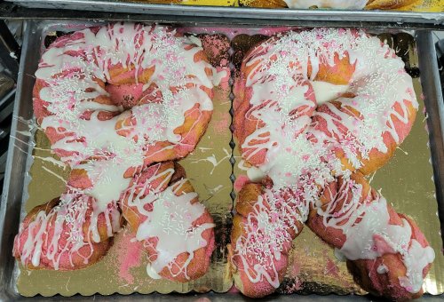 Two large, pink frosted pastries shaped like the number 91, decorated with white icing and sprinkles on a gold tray.