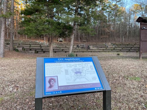 A sign for the CCC Amphitheater in a wooded area, with seating rows visible in the background.