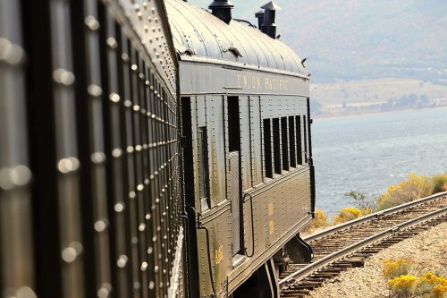 A vintage train car labeled "Indian Pacific" travels along a scenic lakeside track.