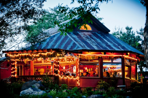 A cozy restaurant with a rustic design, adorned with string lights and surrounded by trees, creating a warm atmosphere.