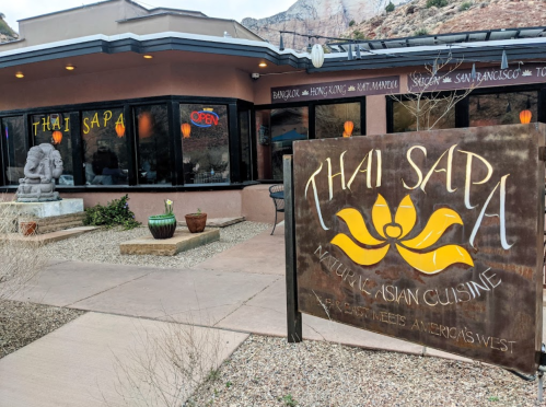 Exterior of Thai Sapa restaurant featuring a sign, decorative lanterns, and a statue in a landscaped area.
