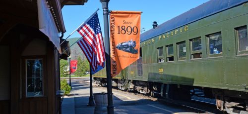 A train station with an American flag and an orange banner reading "Since 1899" next to a green train car.