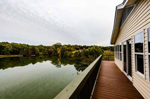 A wooden deck overlooks a calm lake surrounded by trees under a cloudy sky.