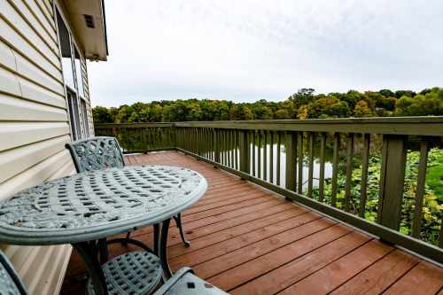 A balcony with a round table and chairs overlooking a serene lake surrounded by trees.