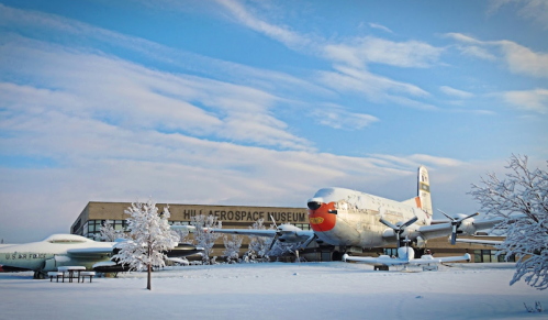 A snowy scene featuring the Hill Aerospace Museum with a vintage aircraft displayed outside.