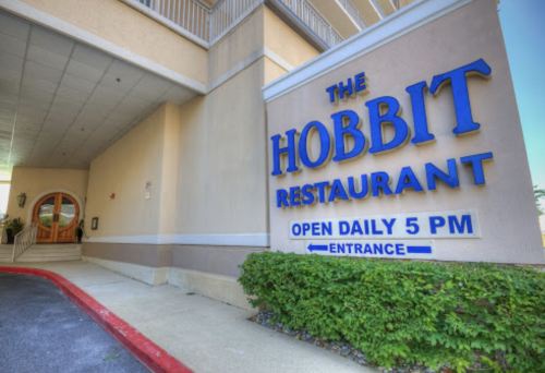 Sign for "The Hobbit Restaurant" with an entrance, featuring blue lettering and a welcoming atmosphere. Open daily at 5 PM.