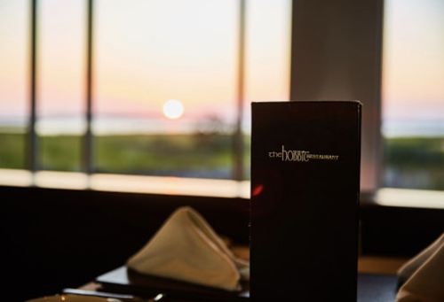 A restaurant menu stands in the foreground with a sunset view through large windows in the background.
