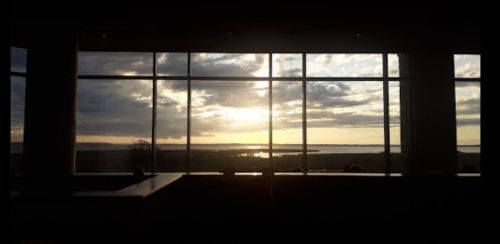 Sunset view through large windows, with clouds and water visible in the distance, creating a serene atmosphere.