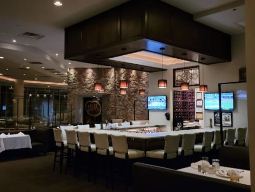 A modern restaurant interior featuring a stone wall, bar seating, and multiple screens displaying sports.