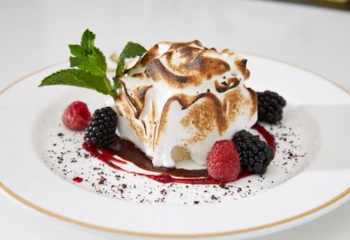 A dessert featuring a toasted meringue topping, surrounded by raspberries, blackberries, and a berry sauce.