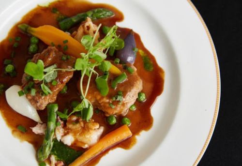 A gourmet dish featuring meatballs, vibrant vegetables, and a rich sauce, garnished with fresh herbs on a white plate.