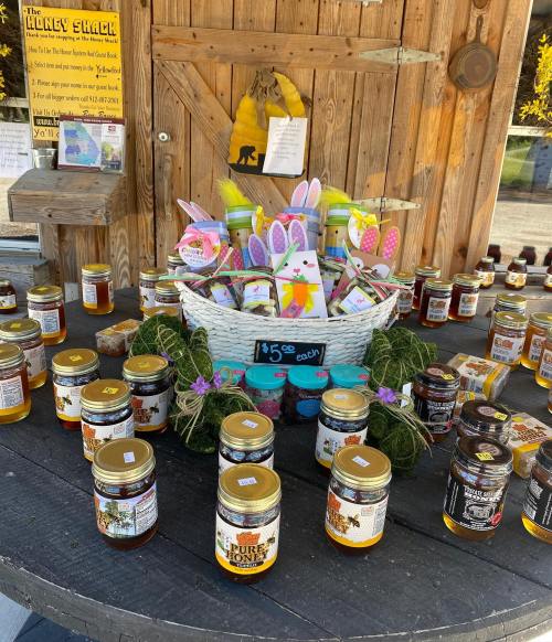 A display of various honey jars and a basket with colorful Easter decorations on a wooden table.