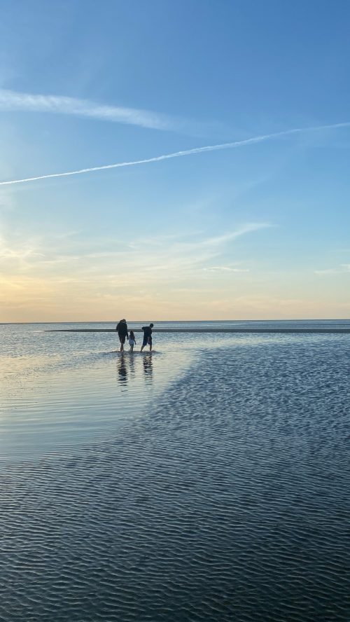 Two people walking on a shallow beach at sunset, with calm water reflecting the sky.