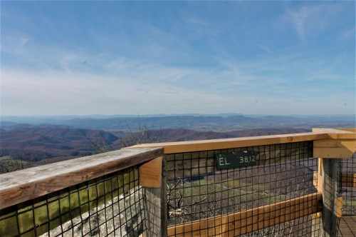 A scenic view from a lookout point, featuring rolling hills and a clear blue sky.