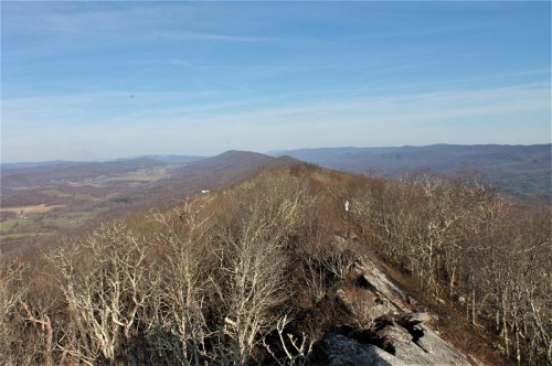 A panoramic view of a mountainous landscape with bare trees and rolling hills under a clear blue sky.