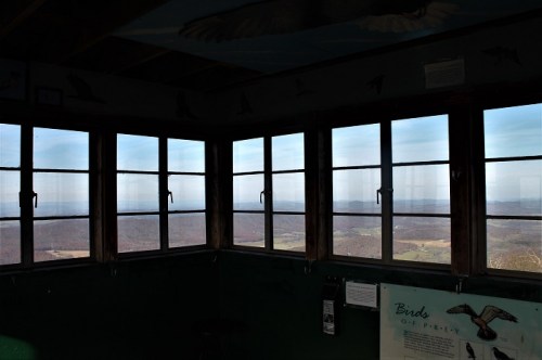Interior of a lookout tower with multiple windows showcasing a distant landscape and blue sky.