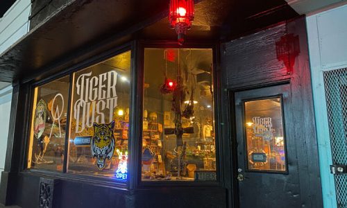 A storefront at night with a glowing "Tiger Dust" sign, featuring a tiger graphic and warm interior lighting.