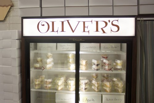 A display case labeled "Oliver's" filled with various desserts, including pies and custards, neatly arranged inside.