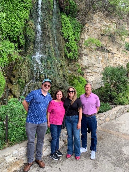 Four people stand in front of a waterfall and lush greenery, smiling for the camera.