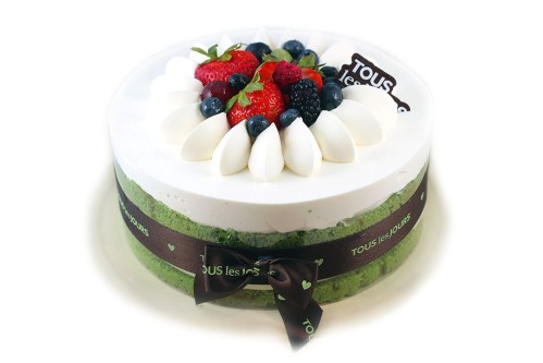 A round cake topped with strawberries, blueberries, and white cream, decorated with a chocolate sign and a ribbon.