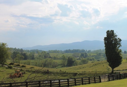 A scenic landscape featuring rolling hills, a distant mountain range, and a wooden fence under a cloudy sky.