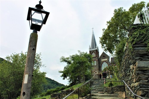A stone pathway leads up to a church with a tall spire, surrounded by greenery and a vintage lamp post nearby.