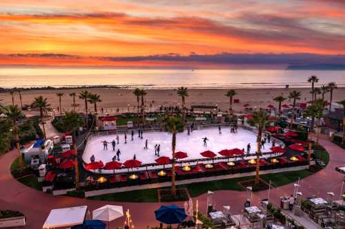 A vibrant sunset over a beachside ice skating rink surrounded by palm trees and red umbrellas.