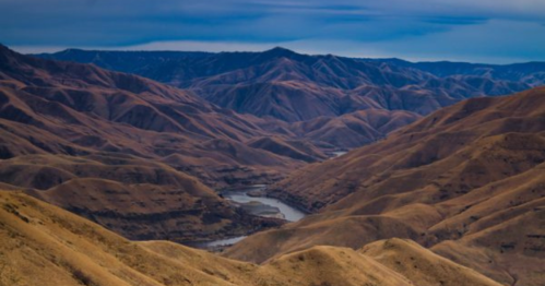 A panoramic view of rolling, golden hills with a winding river nestled in the valley below under a blue sky.