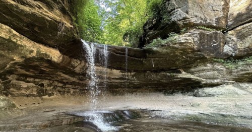 A serene waterfall cascades over rocky cliffs into a tranquil pool, surrounded by lush green foliage.