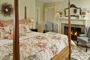 Cozy bedroom with a floral bedspread, two armchairs, and a fireplace, creating a warm and inviting atmosphere.