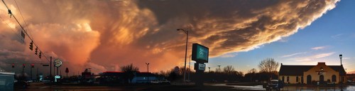 A dramatic sunset sky with swirling clouds over a cityscape, featuring a fast-food restaurant and a church.