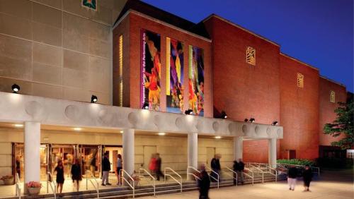 A modern building exterior at dusk, featuring colorful artwork and people entering through the front entrance.